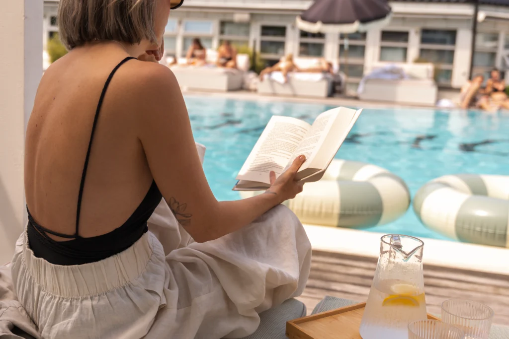 Gäst som sitter vid poolen och läser bok på Ystad Saltsjöbad, spa- och poolmiljö i Skåne.