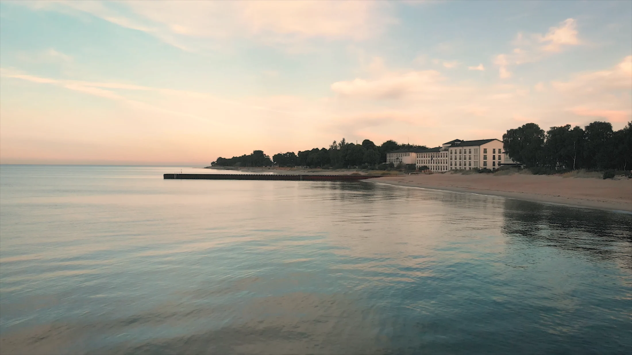 Flygvy över Ystad Saltsjöbad vid havet i solnedgång med strand, brygga och hotellbyggnad.